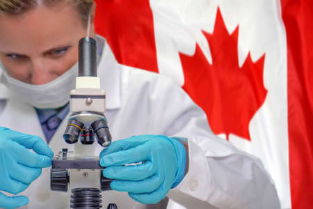 Female biochemist looking through a microscope against Canada flag background. Medical technology and pharmaceutical research and development of science concept in Canadaの写真素材