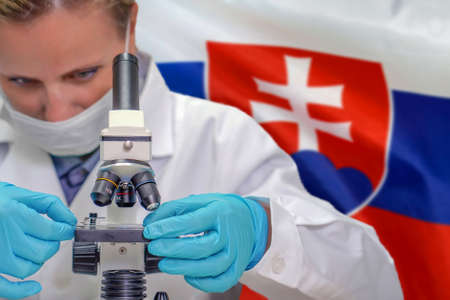 Female biochemist looking through a microscope against Slovakia flag background. Medical technology and pharmaceutical research and development of science concept in Slovakiaの写真素材