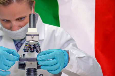 Female biochemist looking through a microscope against Italy flag background. Medical technology and pharmaceutical research and development of science concept in Italyの写真素材