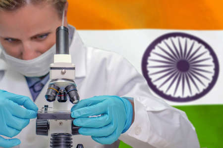 Female biochemist looking through a microscope against India flag background. Medical technology and pharmaceutical research and development of science concept in Indiaの写真素材