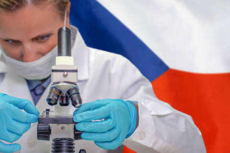 Female biochemist looking through a microscope against Czech Republic flag background. Medical technology and pharmaceutical research and development of science concept in Czech Republicの写真素材