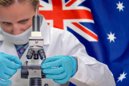Female biochemist looking through a microscope against Australia flag background. Medical technology and pharmaceutical research and development of science concept in Australiaの写真素材