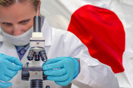 Female biochemist looking through a microscope against Japan flag background. Medical technology and pharmaceutical research and development of science concept in Japanの写真素材