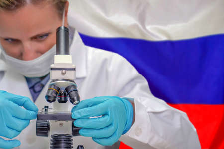 Female biochemist looking through a microscope against Russia flag background. Medical technology and pharmaceutical research and development of science concept in Russiaの写真素材