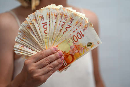 In the hands of a lot Israeli money, denominations of 100 sheqel. Woman hands hold fan of new Israeli money bills (banknotes) of 100 shekelの写真素材