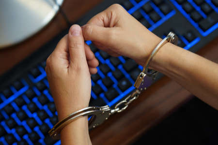 Hands of arrested woman hacker in handcuffed on compuer keyboard. Prisoner or arrested terrorist,...
