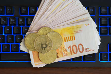 Bitcoin and new Israeli money bills (banknotes) of 100 shekel on compuer keyboard. Symbol of electronic virtual money and mining cryptocurrency conceptの写真素材