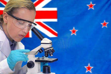 Female biochemist mixing substances to study under the microscope against New Zealand flag...