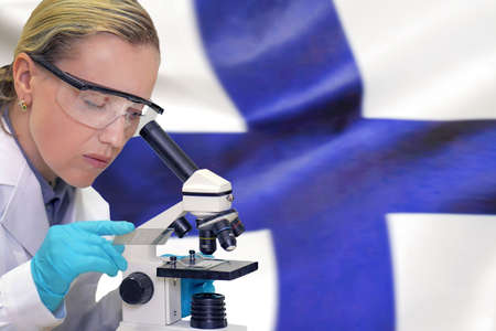 Female biochemist mixing substances to study under the microscope against Finland flag background. Medical technology and pharmaceutical research and development of science concept in Finlandの写真素材