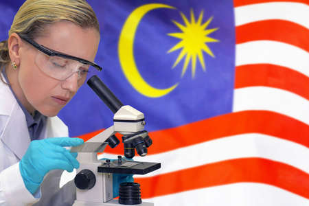 Female biochemist mixing substances to study under the microscope against Malaysia flag background. Medical technology and pharmaceutical research and development of science concept in Malaysiaの写真素材