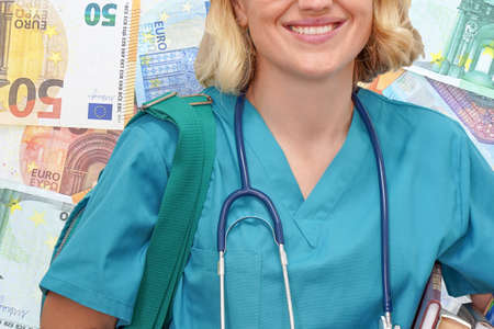 Woman student doctor with stethoscope and books in hand on the background of the stack of Euro banknotes. Medical education concept. Expensive medical learningの写真素材