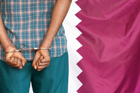 African man with handcuffs on the background of the Qatar flag. back view. Concept of prisons and corruption in Qatarの写真素材