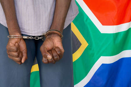 African man with handcuffs on the background of the South Africa flag. back view. Concept of prisons and corruption in South Africaの写真素材