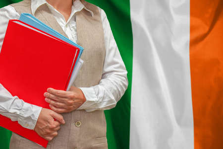 Woman holding red folder on Ireland flag background. Education and jurisprudence concept in Irelandの写真素材