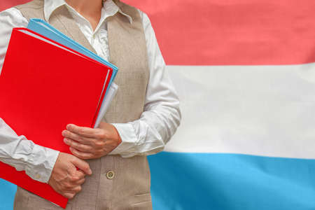 Woman holding red folder on Luxembourg flag background. Education and jurisprudence concept in Luxembourgの写真素材