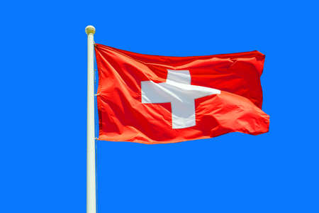Switzerland flag waving against clean blue sky, close up. Swiss flag in the blue sky. Flag Switzerland on blue sky backgroundの写真素材