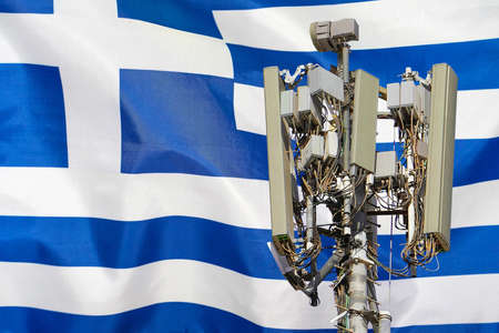Telecommunications tower with a 5G cellular network antenna agains flag of Greece. Telecommunication tower of 5G cellular communication. 5G technology usage on telecommunications towers in Greeceの写真素材