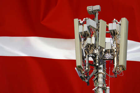 Telecommunications tower with a 5G cellular network antenna agains flag of Latvia. Telecommunication tower of 5G cellular communication. 5G technology usage on telecommunications towers in Latviaの写真素材