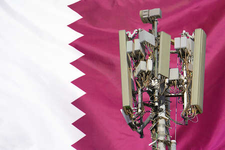 Telecommunications tower with a 5G cellular network antenna agains flag of Qatar. Telecommunication tower of 5G cellular communication. 5G technology usage on telecommunications towers in Qatarの写真素材
