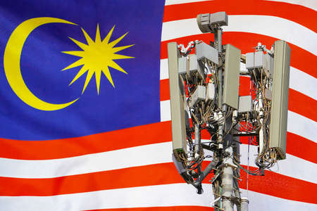 Telecommunications tower with a 5G cellular network antenna agains flag of Malaysia....