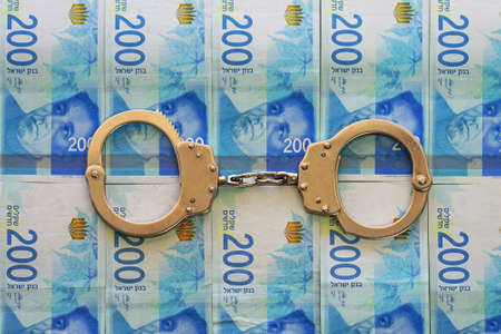 Handcuffs on the background of Israeli 200 banknote money. Police handcuffs. Financial crime, dirty money and corruption concept. New Israeli Shekel series Cの写真素材