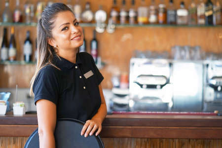 Portrait of waitress standing near the restaurant bar of the hotel. A waitress with a tray is waiting for the orderの写真素材