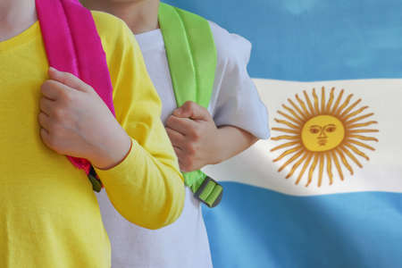 Two children with satchels background of Argentina flag. Concept of upbringing and educating children in Argentinaの写真素材