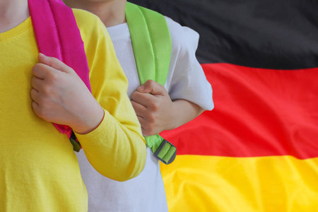 Two children with satchels background of Germany flag. Concept of upbringing and educating children in Germanyの写真素材