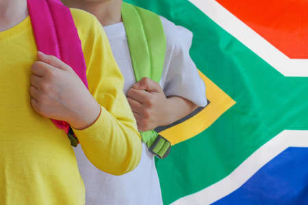 Two children with satchels background of South Africa flag. Concept of upbringing and educating children in South Africaの写真素材