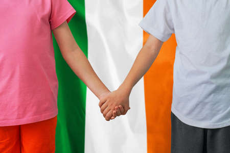 Two children joined hands on flag Ireland background. Boy and girl joined hands on background flag of Ireland. Concept of family and parenting in Irelandの写真素材