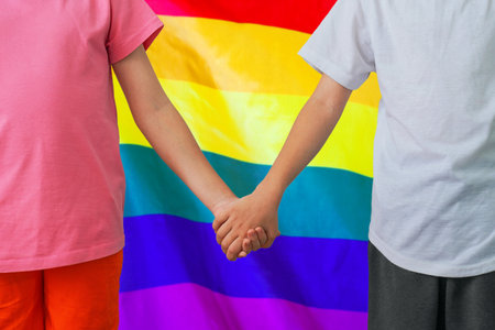 Two children joined hands on rainbow flag background. Boy and girl joined hands on background flag of LGBT. Concept of upbringing children LGBTの写真素材