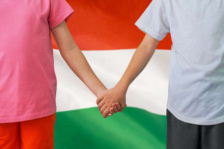 Two children joined hands on flag Hungary background. Boy and girl joined hands on background flag of Hungary. Concept of family and parenting in Hungaryの写真素材
