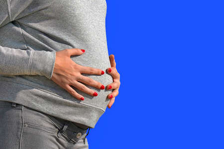 Closeup pregnant woman touching her belly on blue sky background. Healthy Pregnancy concept, Gravid female on blue sky background. Copy space for text messagesの写真素材