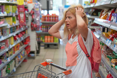 Upset woman in a supermarket with an empty shopping trolley. Crises, rising prices for goods and...