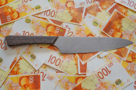 Money with a knife. Knife on pile of new Israeli money bills (banknotes) of 100 shekel background