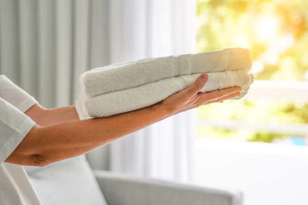 Hands of housekeeping woman an hotel holding fresh clean folded towels for the room. Chambermaid hands woman holding clean towels in hotel roomの写真素材