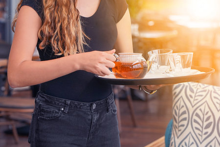 Waitress holding tray with cup of tea and tea glass teapot. Concept of maintenance and serviceの写真素材