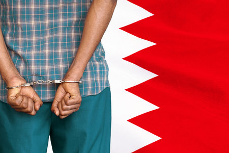 African male with handcuffs on the background of the Bahrain flag. back view. Concept of prisons and corruption in Bahrainの写真素材