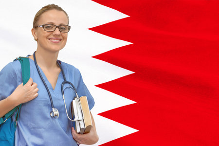 Female student doctor with stethoscope and books in hand on the Bahrain flag background. medical education concept. medical training in Bahrainの写真素材