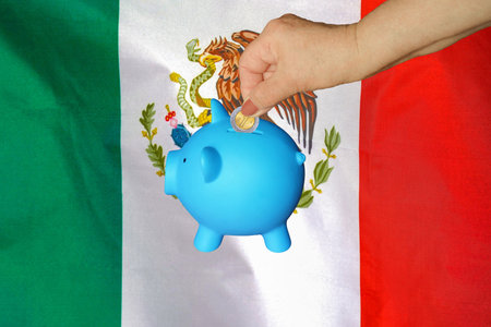 Hand of elderly woman putting coin into piggy bank on Mexico flag background. Hand putting coin to piggy bank. Retirement savings, piggy bank. Concept saving money and retirement fund in Mexicoの写真素材