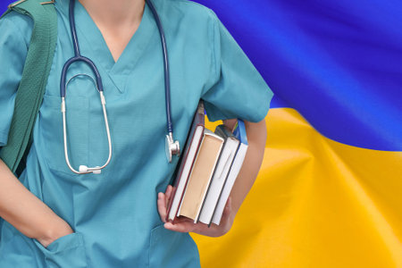 Close-up young female student doctor with stethoscope and books in hand on Ukraine flag background. Nurse, Student, Education. Medical woman student at the university. Medical education in Ukraineの写真素材