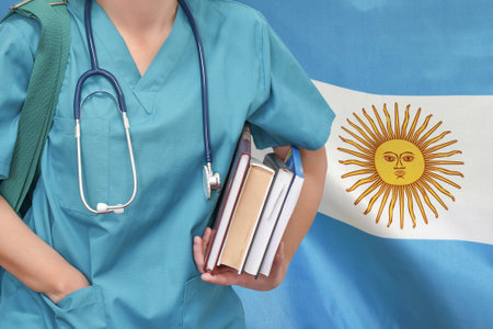 Close-up young female student doctor with stethoscope and books in hand on Argentina flag background. Nurse, Student, Education. Medical woman student at the university. Medical education in Argentinaの写真素材