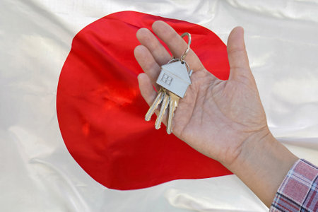 Hand shows the keys to the apartment on background of flag Japan. Keys to the apartment in a female hand on background of flag Japan. Realty concept and home buying or new apartment in Japanの写真素材