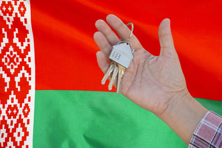 Hand shows the keys to the apartment on background of flag Belarus. Keys to the apartment in a female hand on background of flag Belarus. Realty concept and home buying or new apartment in Belarusの写真素材