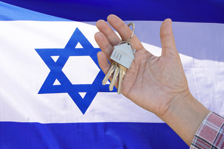 Hand shows the keys to the apartment on background of flag Israel. Keys to the apartment in a female hand on background of flag Israel. Realty concept and home buying or new apartment in Israelの写真素材