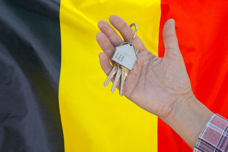 Hand shows the keys to the apartment on background of flag Belgium. Keys to the apartment in a female hand on background of flag Belgium. Realty concept and home buying or new apartment in Belgiumの写真素材