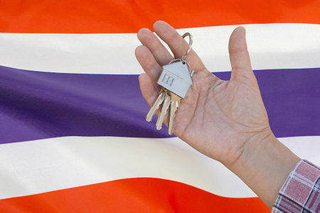 Hand shows the keys to the apartment on background of flag Thailand. Keys to the apartment in a female hand on background of flag Thailand. Realty concept and home buying or new apartment in Thailandの写真素材