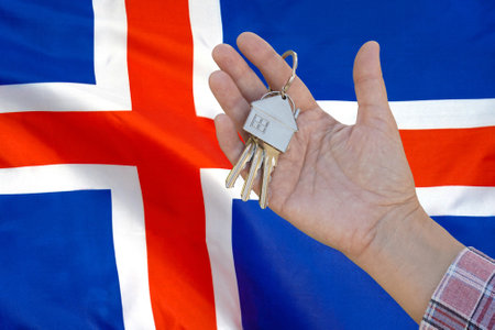 Hand shows the keys to the apartment on background of flag Iceland. Keys to the apartment in a female hand on background of flag Iceland. Realty concept and home buying or new apartment in Icelandの写真素材