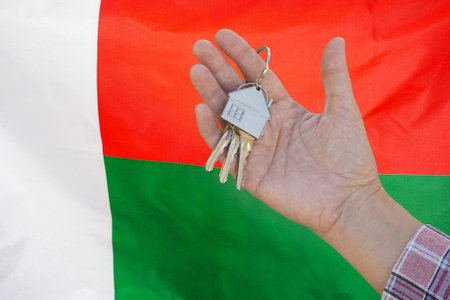 Hand shows the keys to the apartment on background of flag Madagascar. Keys to the apartment in a female hand on background of flag Madagascar. Realty concept new apartment in Madagascarの写真素材