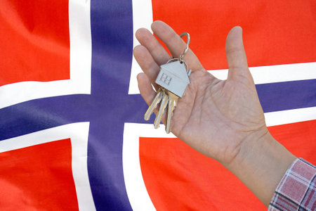 Hand shows the keys to the apartment on background of flag Norway. Keys to the apartment in a female hand on background of flag Norway. Realty concept and home buying or new apartment in Norwayの写真素材